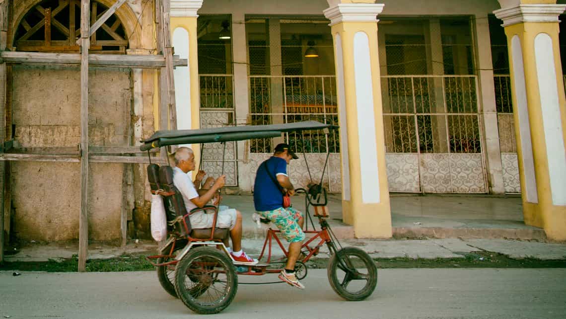 Bicitaxi con turistas, al fondo solares en la zona de la Habana Vieja