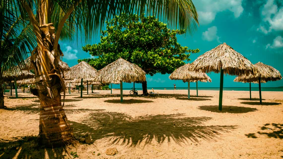 Rusticas sombrillas de playa entre cocoteros en la Playa Ancon al sur de Trinidad