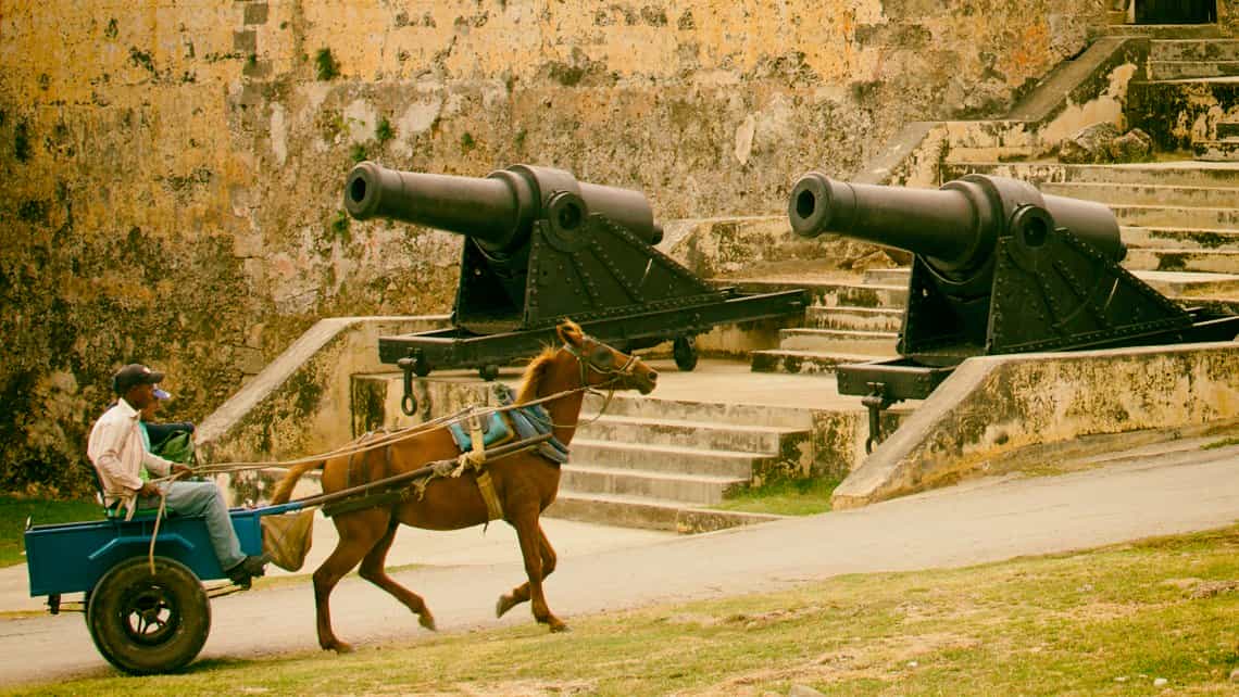 Coche tirado por caballos circula apaciblemente, al fondo el Castillo de Jagua en Cienfuegos