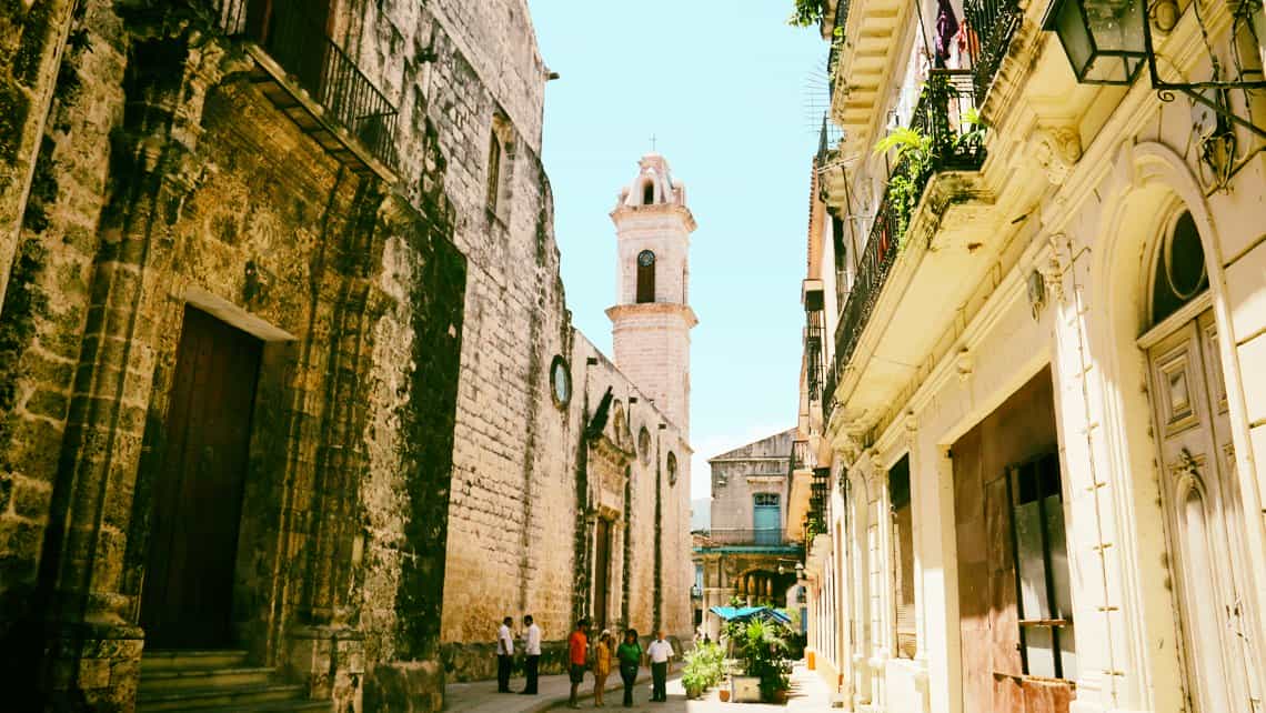 Turistas con guia caminan por las calles de la Habana Vieja, al fondo el campanario de la Catedral de la Habana