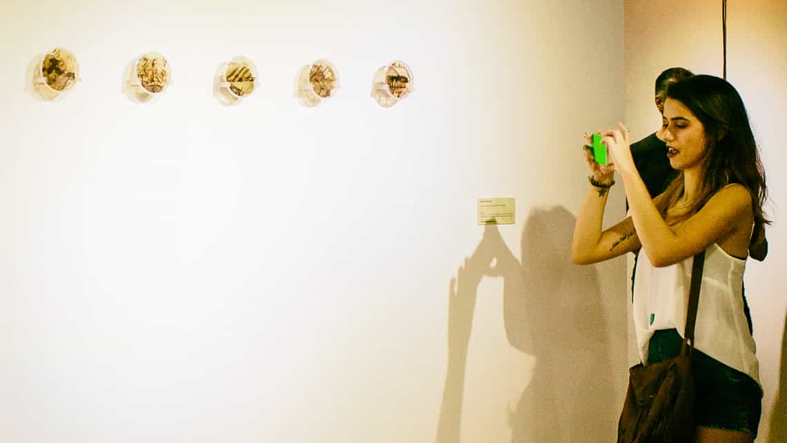 Joven habanera toma fotos de una de las obras en exhibicion en una galeria de arte del Vedado habanero
