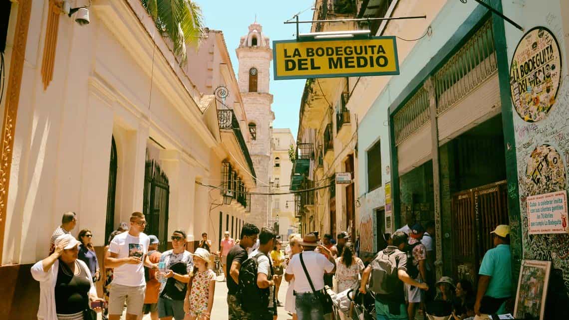 Turistas se toman fotos en la entrada del La Bodeguita del Medio, al fondo el campanario de la Catedral de La Habana