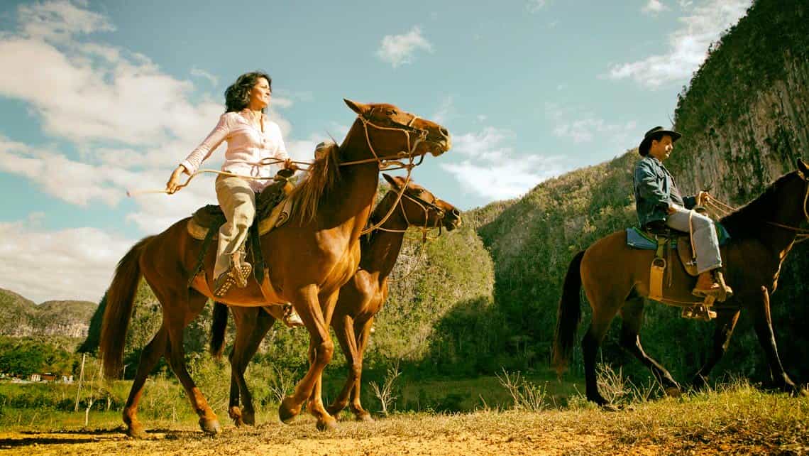 Turistas pasean a caballo por el Valle de Viñales, al fondo los famosos mogotes tipicos de la zona