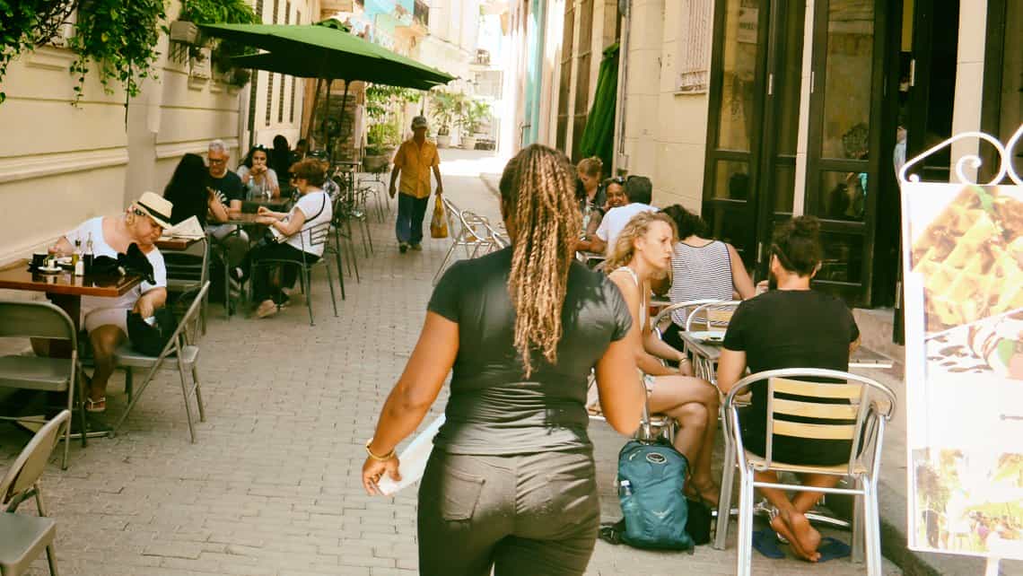 Camarera se aproxima con bebidas a turistas en un bar de La Habana Vieja