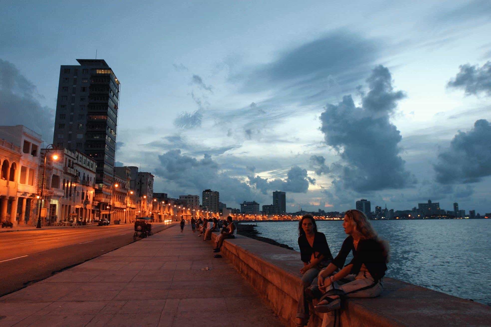 Chicas conversan sentandas en el muro del Malecon durante una bella puesta del sol en La Habana