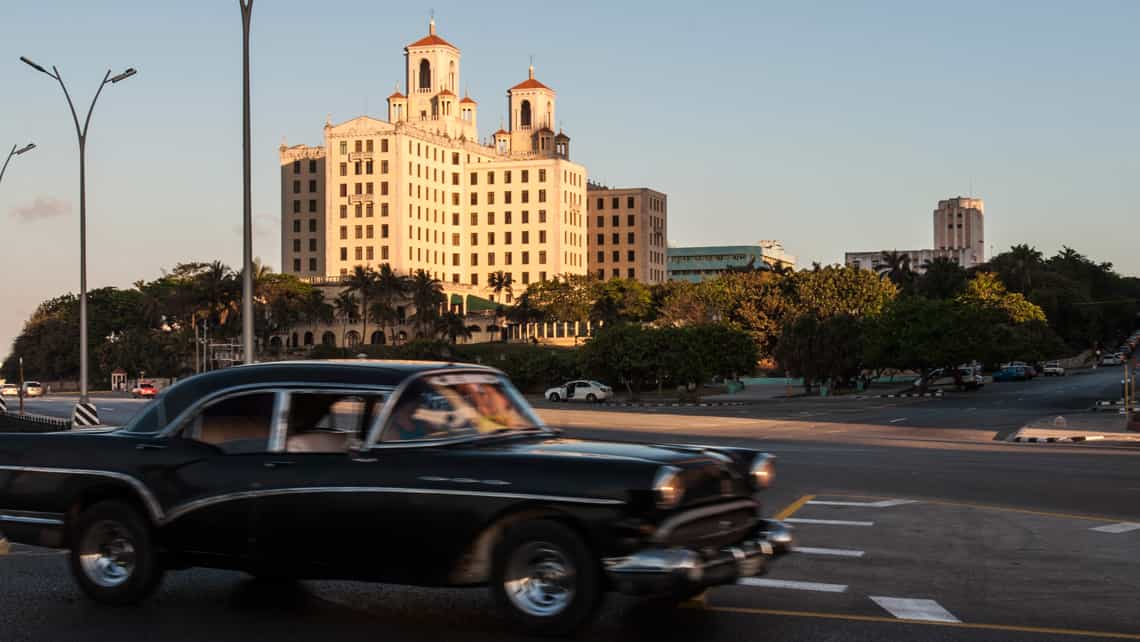 Coche americano de los anos 50 circula por el Malecon habanero, al fondo el Hotel Nacional de Cuba