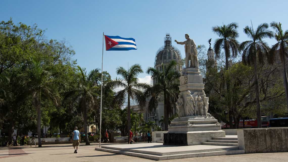 Estatua de Jose Marti en el Parque Central de La Habana Vieja, al fondo ondea la bandera de Cuba