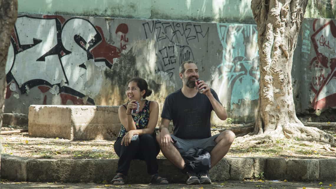 Dos jovenes toman cerveza a la sombra de un arbol en La Habana
