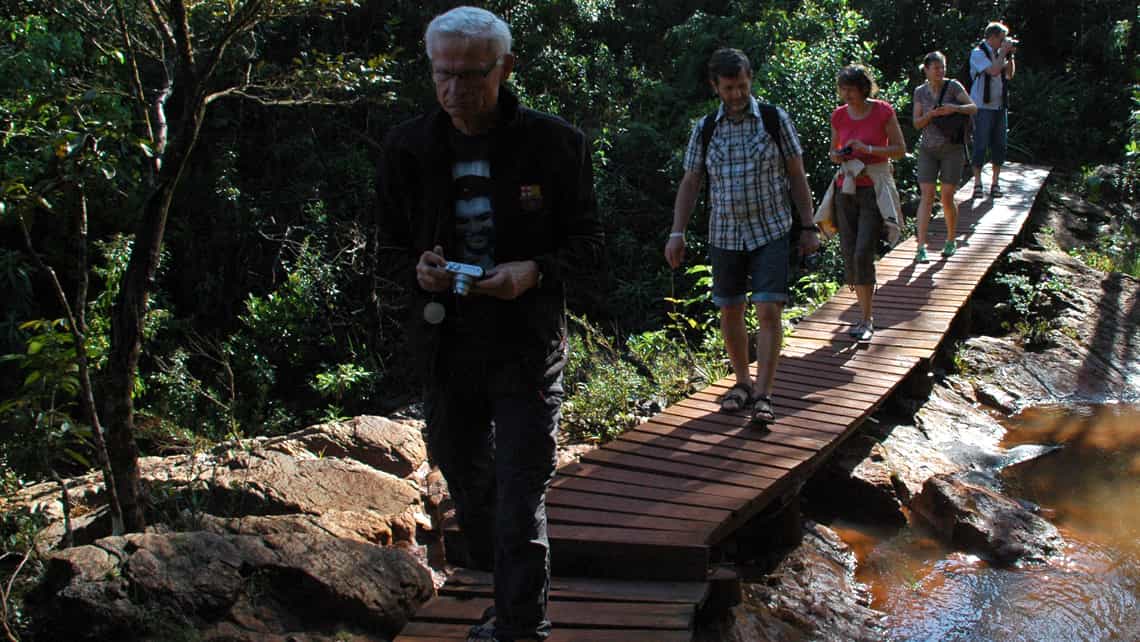Turistas caminan por un puente de madera para cruzar el rio