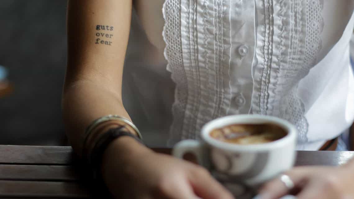 Chica con un tatuaje en el brazo disfruta de un cafe 