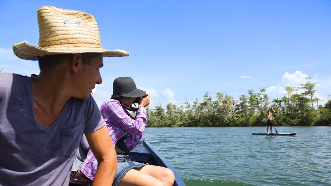 Turistas toman fotos y saludan a una persona que navega en canoa por el rio Toa