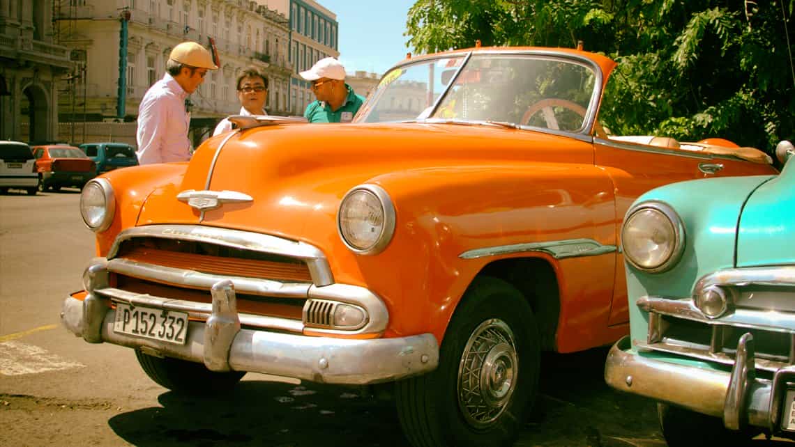 Turistas conversando con el chofer de un coche clasico que ofrece servicio de taxi