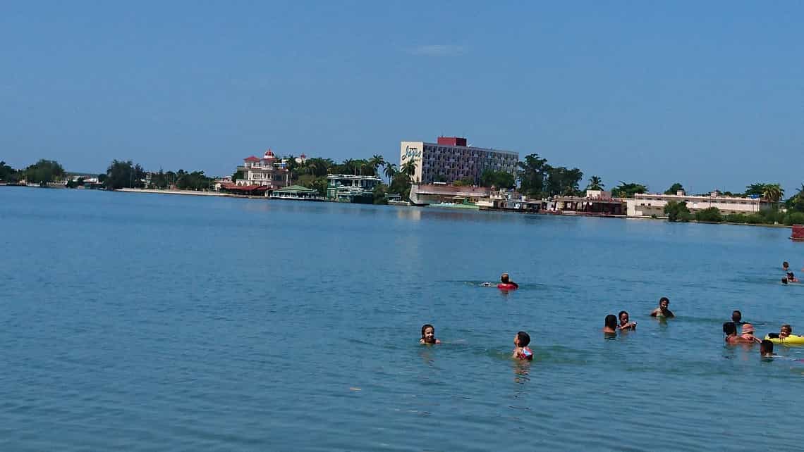 Bañistas disfrutan en la playa de La Laguna del Cura al fondo el Hotel Jagua y Palacio de Valle