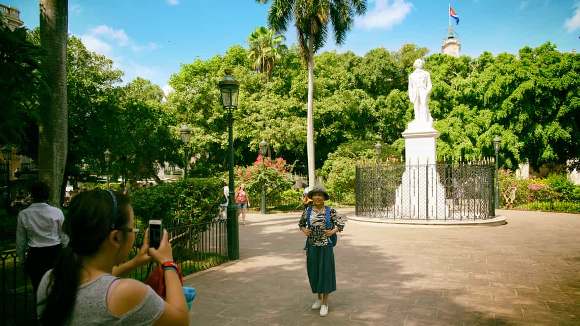 Viajera se toma foto en la Plaza de Armas, al fondo la bandera cubana