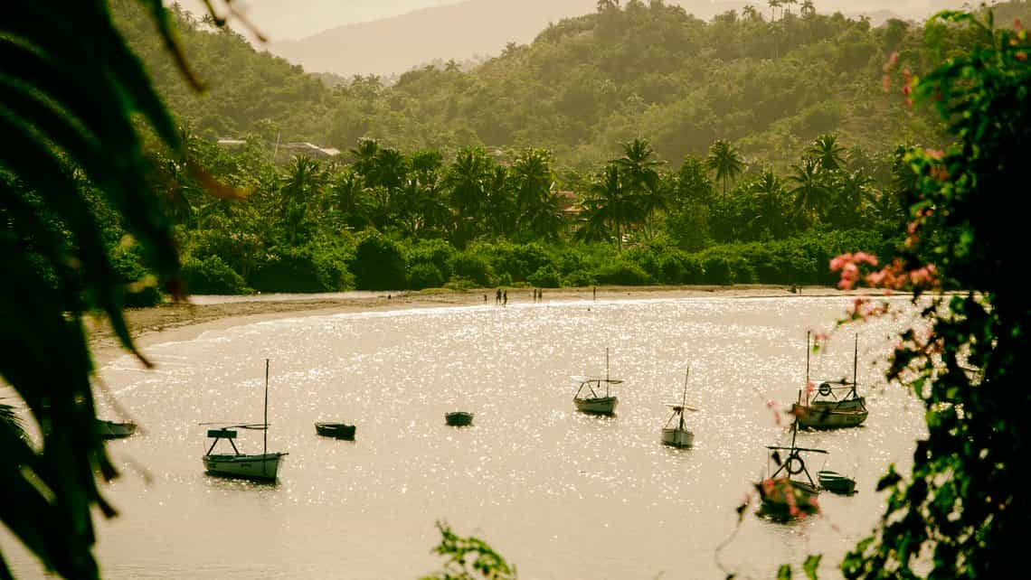 Vista de botes y personas en las aguas de la Playa Baracoa, al fondo la colinas cubiertas de vegetacion
